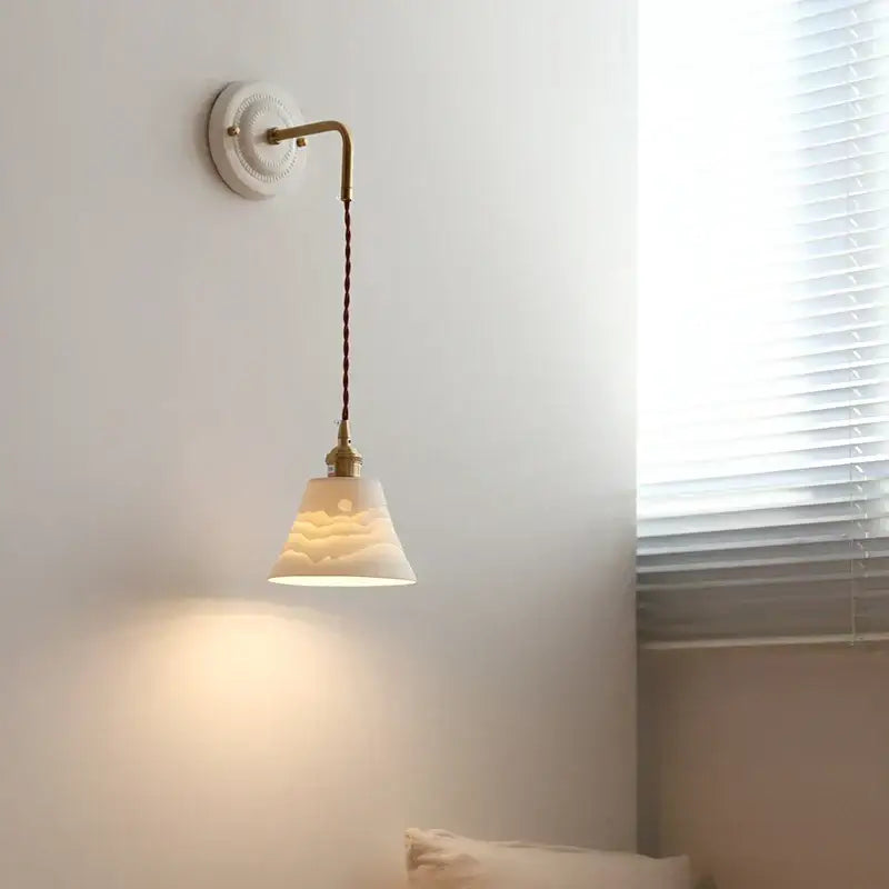 Delicate off-white ceramic wall sconce with brass arm and adjustable led light featuring wave-like etchings decorbites adjustable led