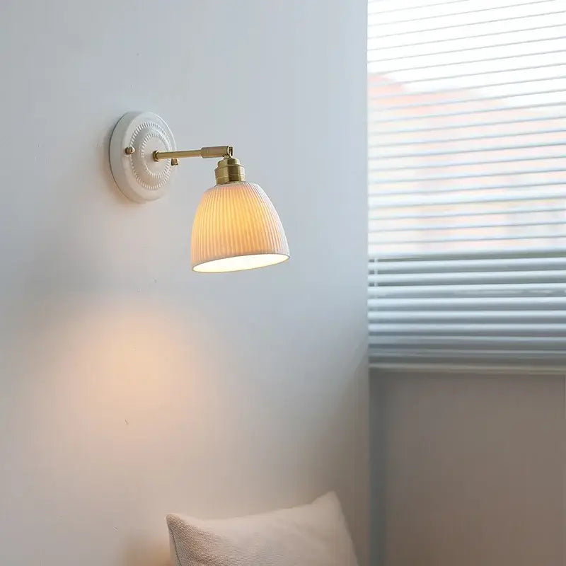 Vintage warm-toned ribbed ceramic and brass wall sconce light with pull chain mounted on white circular wall plate