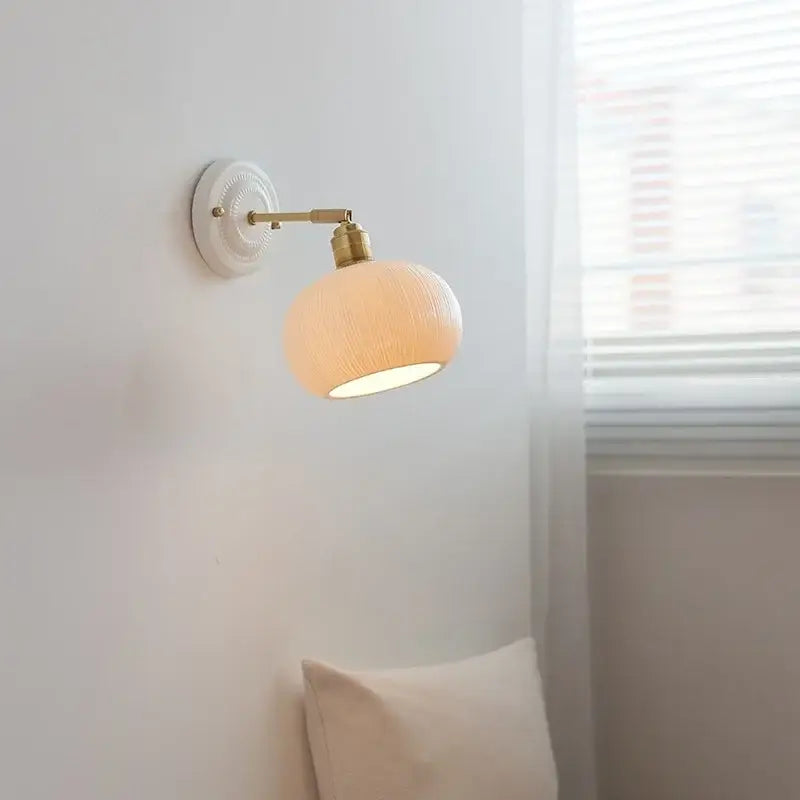 A warm-toned vintage ceramic wall sconce light with a brass arm and pull chain for bedroom use