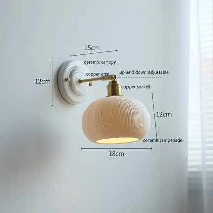Cream-colored decorbites ceramic wall lamp with ribbed ceramic shade and brass-finished copper arm for bedroom decor