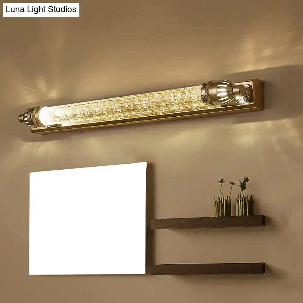Gold-toned wall-mounted vanity light with textured sparkling glass tube and ornate metal ends for bathroom use