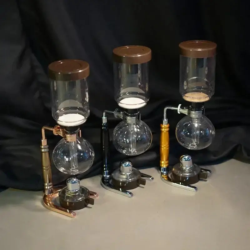 Three glass decorbites coffee jug siphon makers with brown lids and copper black and gold metallic bases for kitchen use