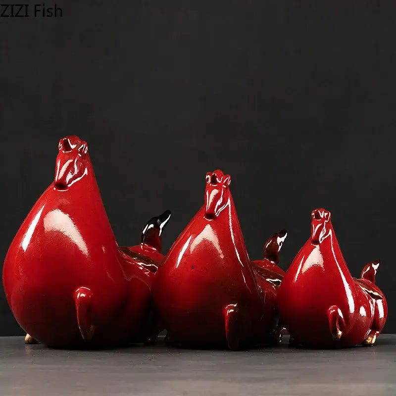 Three glossy red ceramic chicken figurines with black beaks and gold feet beside a vintage dark gray horse porcelain statue