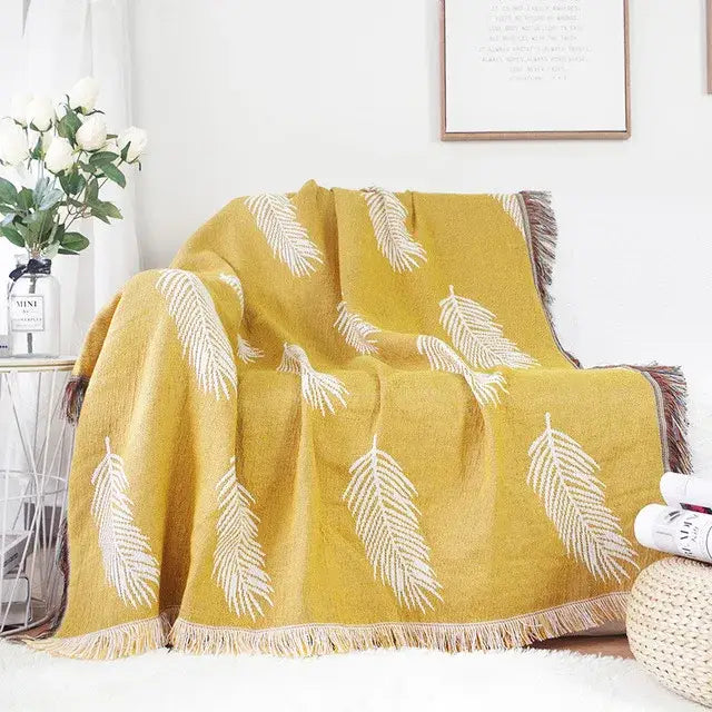 A mustard-yellow bohemian cotton plaid sofa throw blanket with white embroidered feathers and fringed edges by decorbites bohemian cotton