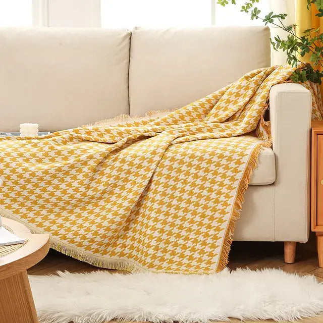 A cozy mustard-yellow and cream decorbites bohemian cotton plaid sofa blanket with fringed edges draped over beige sofa
