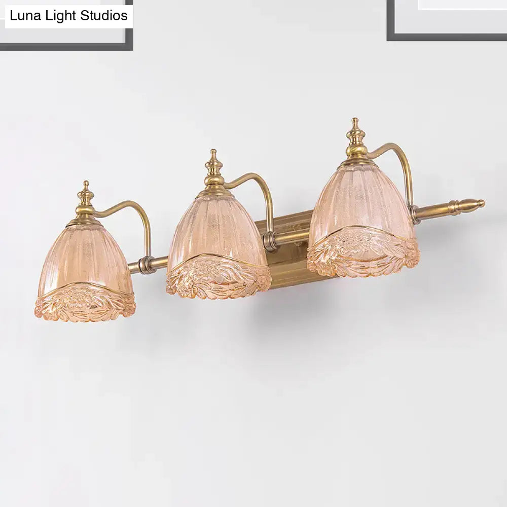 Antique brass three-light vanity fixture with delicate pink frosted floral shades featuring amber glass accents