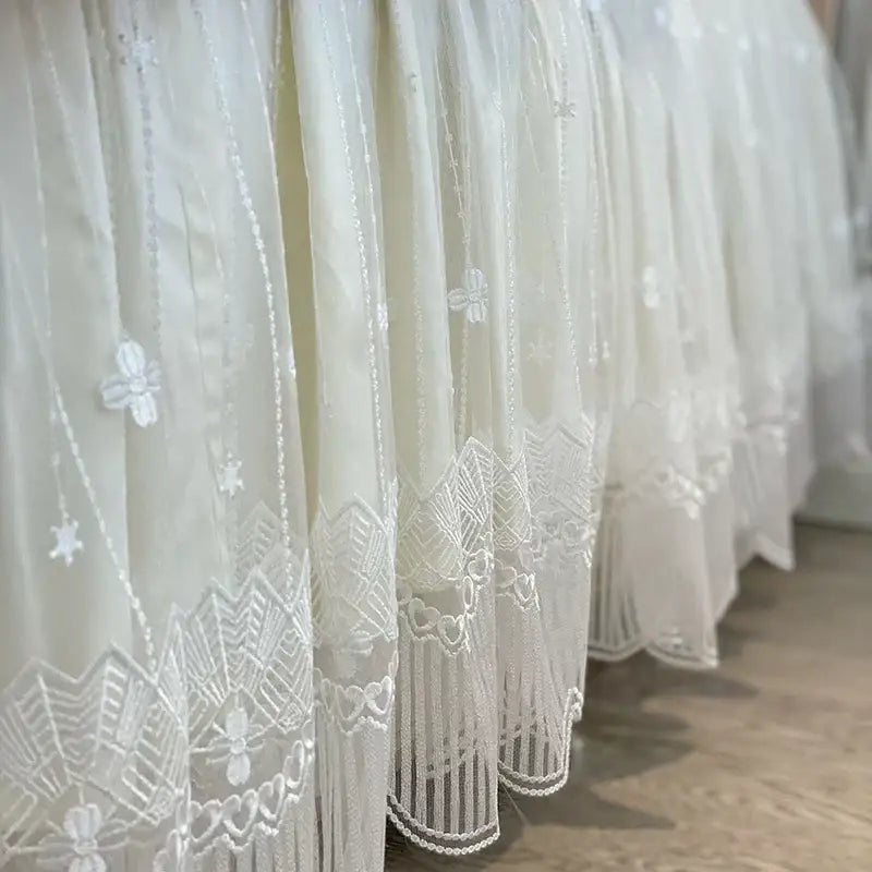 Delicate white lace curtain with intricate floral and geometric embroidery hem in vintage french beige and cream bedding set with ruffles