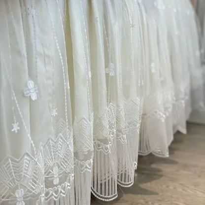 Delicate white lace curtain with intricate floral and geometric embroidery hem in vintage french beige and cream bedding set with ruffles