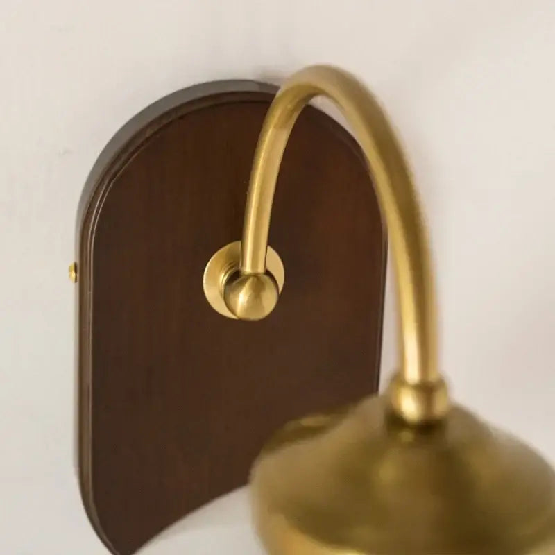 Brass-finished glass copper led wall light with curved arm and dark wood backplate for vintage bedroom lighting