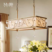 Gold-toned rectangular island pendant with intricate floral metalwork, crystal accents, and woven golden flax shade