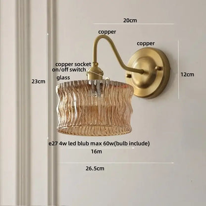 Antique brass-finished copper wall light with textured amber glass shade and copper knob switch for bedroom use