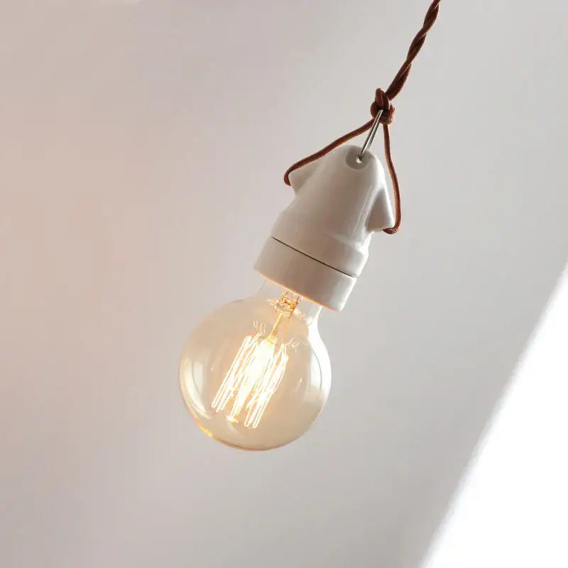 A warm-toned vintage incandescent bulb in a matte white ceramic led pendant lamp with brown twisted cord decorbites ceramic led