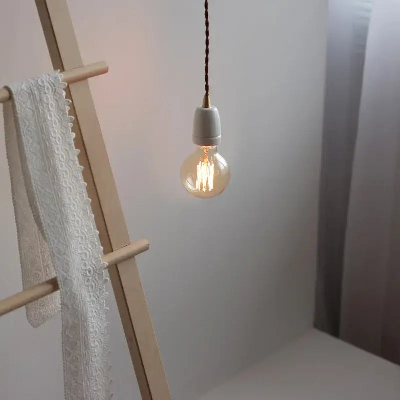 A warm-glowing clear glass filament bulb in vintage industrial matte white ceramic led pendant lamp with twisted cord