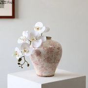 A blush-pink porcelain vase with cracked texture and vintage floral pattern holds white orchids for living room decor