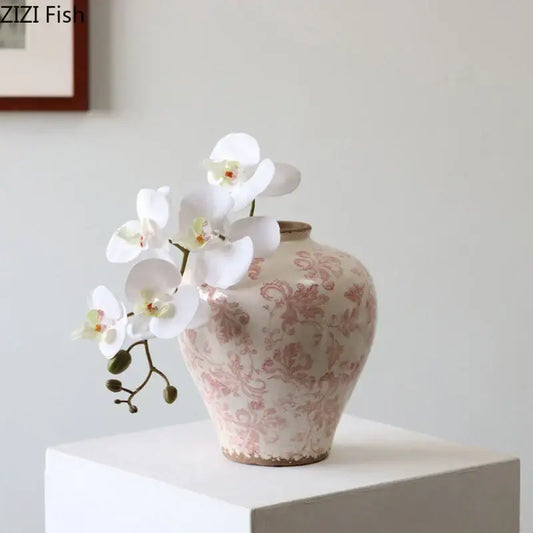 A blush-pink porcelain vase with cracked texture and vintage floral pattern holds white orchids for living room decor