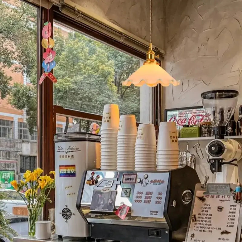 Stacked white disposable coffee cups beside a vintage scalloped decorbites cream glass led pendant light for kitchen dining room