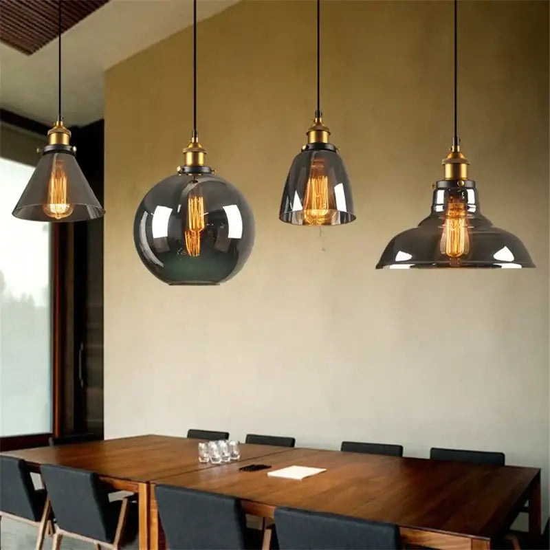 Four vintage-style pendant lights with dark smoked glass ball shades and brass accents hang above a wooden table decorbites glass ball