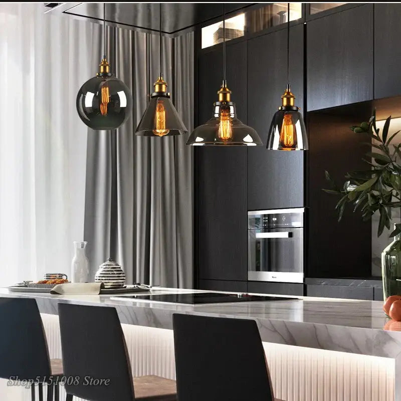 Four vintage-style decorbites smoky grey glass pendant lights with brass accents hang above a modern kitchen island