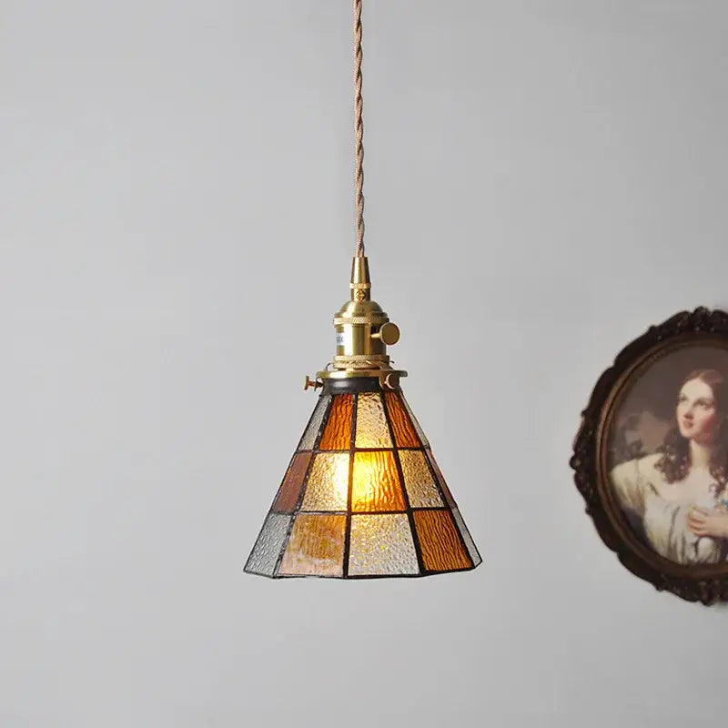 A warm-toned vintage stained glass copper pendant light with a brass fixture and wood knob switch for kitchens