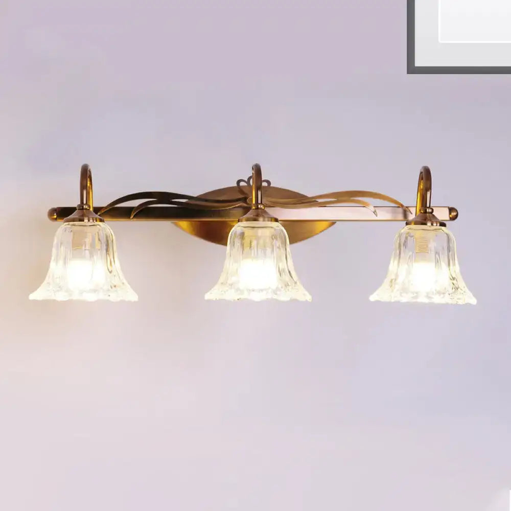 Vintage style wall light with brass finish and three clear bell-shaped glass shades for bathroom vanity use