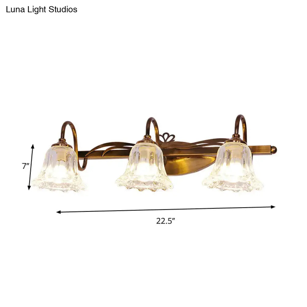 Antique brass three-light vintage style wall light with clear textured glass bell shades for bathroom vanity use
