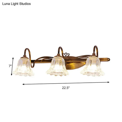 Antique brass three-light vintage style wall light with clear textured glass bell shades for bathroom vanity use