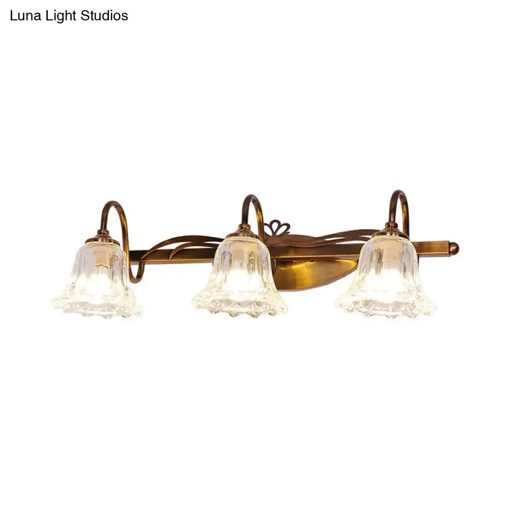 Antique brass three-light vintage style wall light with clear textured glass bell shades for bathroom vanity use