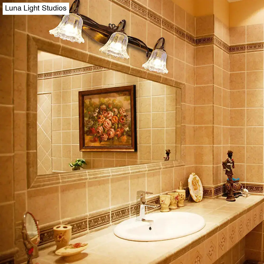 Three-light vintage style wall light with ornate dark metal arms and clear bell-shaped glass shades for bathroom vanity