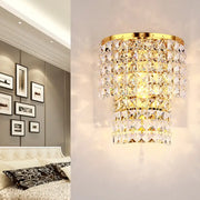 Vintage style wall sconce with gold tone and tiered faceted clear crystals in a cascading design for bedroom light