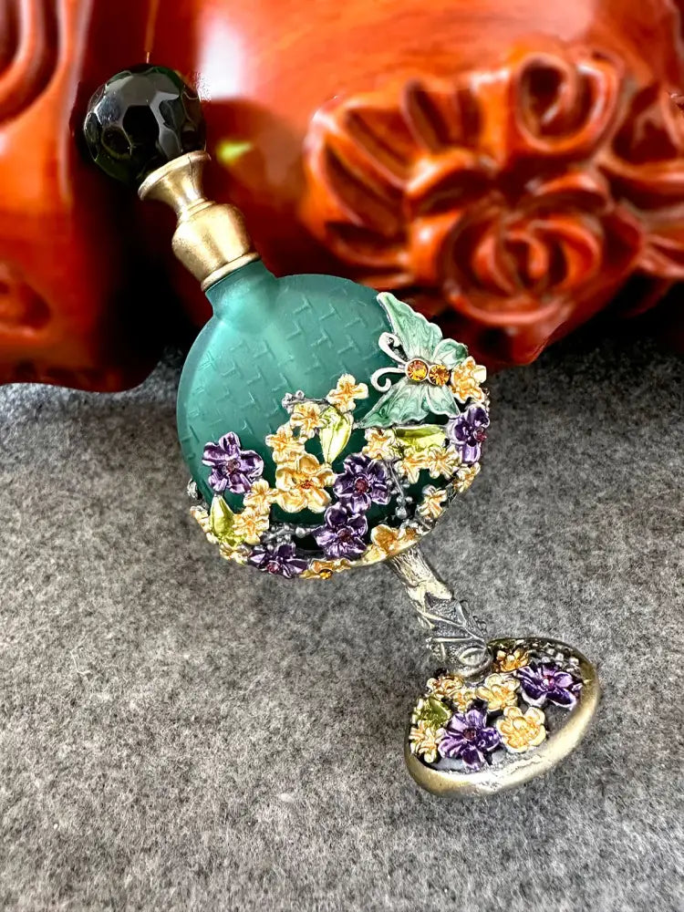 Vintage teal and purple glass perfume bottle with black stopper and floral embellishments for bedroom decor