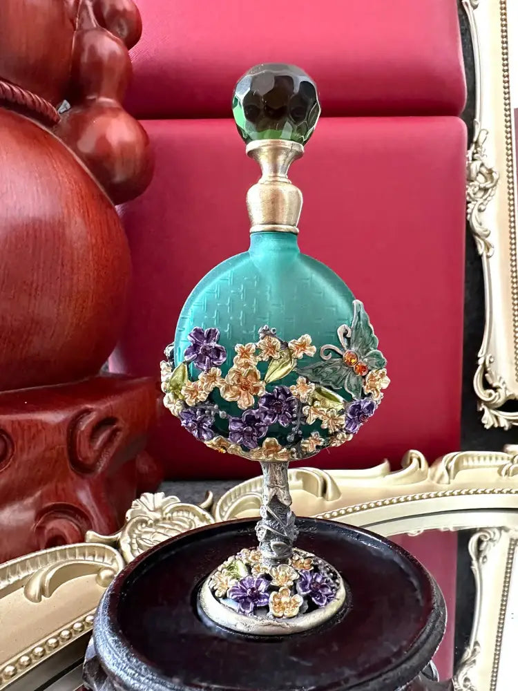 Vintage teal and purple glass perfume bottle with faceted green stopper and ornate floral embellishments for bedroom decor