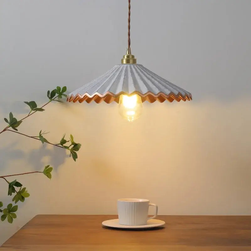 A delicate light gray decorbites ceramic led pendant light with scalloped edge and copper trim above wooden table