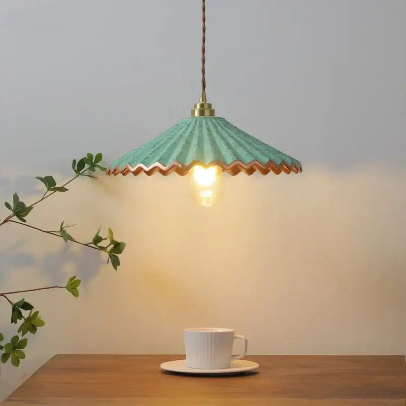 A teal scalloped-edge pendant light with brass fixture and braided cord hangs above a white cup on wood table vintage decorbites ceramic led pendant light