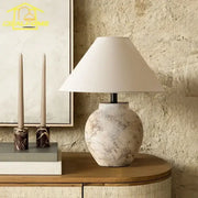 A rustic vintage white and gray ceramic led table lamp with distressed finish and wide off-white conical shade for decorbites decor