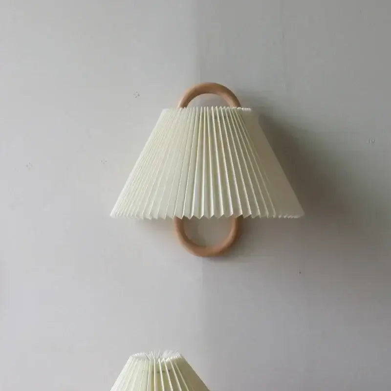 Off-white pleated fabric shade wall lamp mounted on a light beech wood ring for bedroom use