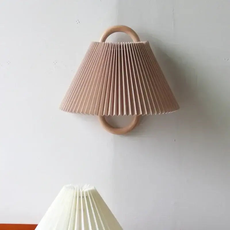 Wabi-sabi beech wood wall lamp with soft blush pink pleated fabric shade and circular wooden handle mounted on white wall