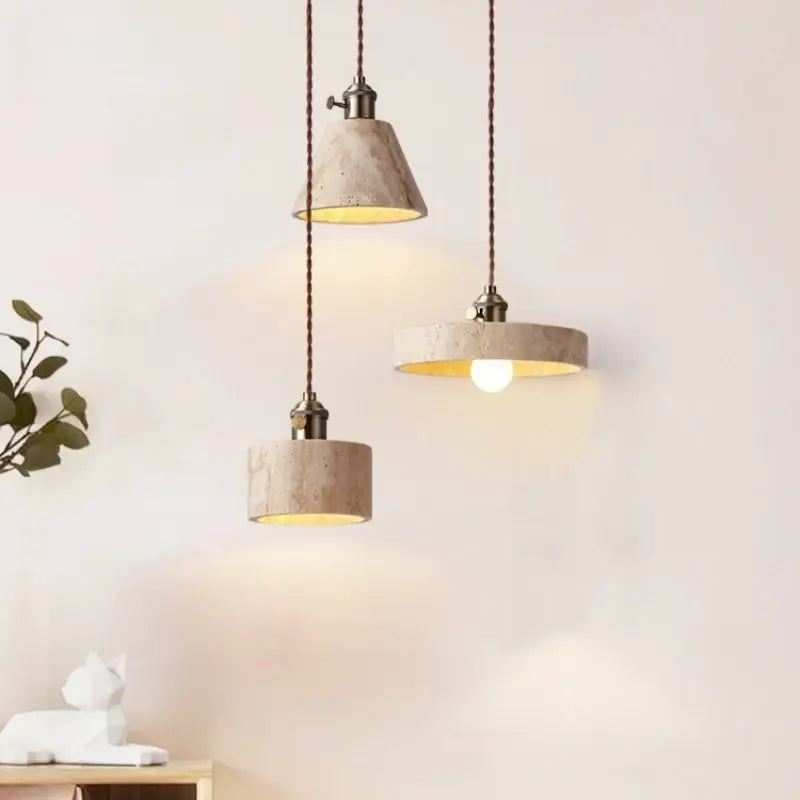 Three beige concrete pendant lights with warm led yellow travertine interiors and dark braided cords for dining room decorbites led yellow