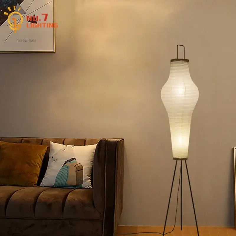 A tall cream paper tripod floor lamp with a white shade and black metal base for living room art decor