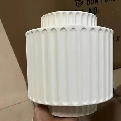 White ceramic vase with vertical fluted ridges in a tiered cylindrical shape for cream white resin wall lamp