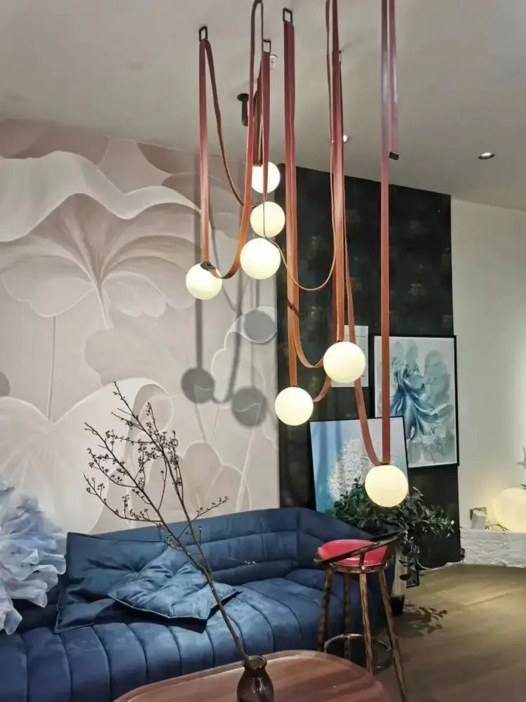 A wabi sabi designer copper and white chandelier with warm spherical bulbs and leather straps for living room duplex