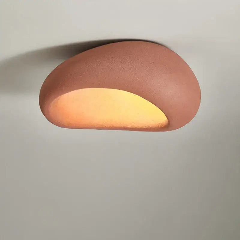 A warm terracotta ceramic wall sconce with smooth curves and glowing light complementing cream ceiling chandelier decor