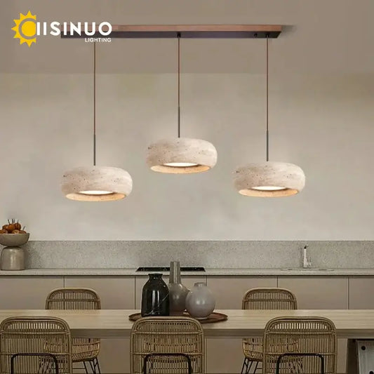 Three modern wabi sabi off white travertine cord pendant lights with textured shades and warm bases hang from a wooden bar