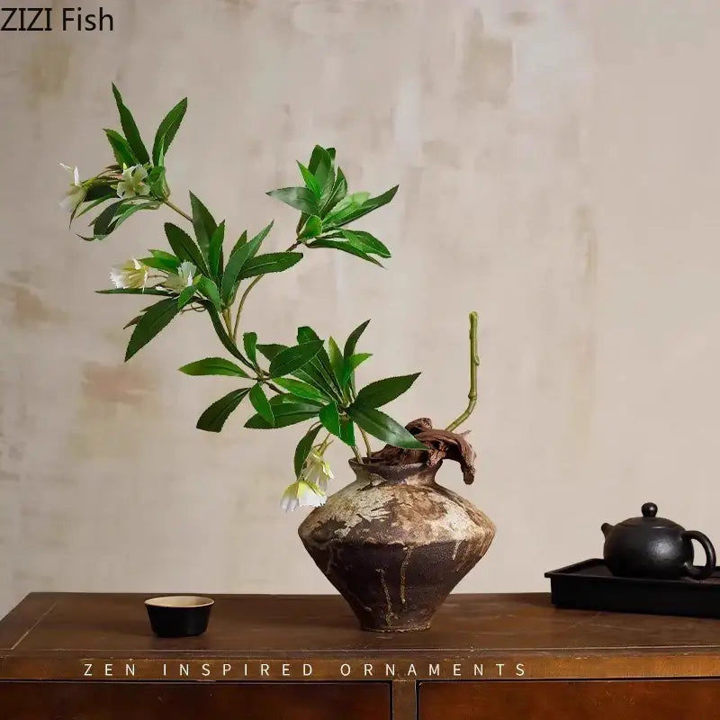 A rustic dark brown decorbites ceramic vase with textured surface holding green leaves and white flowers for living room decor