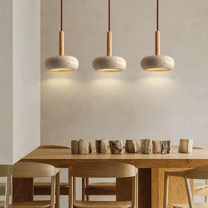 Three minimalist pendant lights with off-white concrete shades and solid wood accents above a wooden dining table