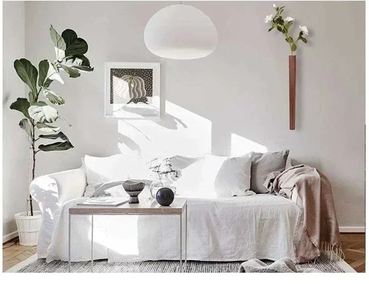 White upholstered sofa with soft draped fabric and white gray pillows beside bohemian style wooden wall hanging vase