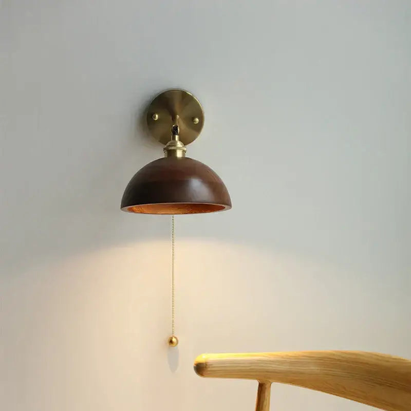Warm-toned brass wall sconce with polished dark wood dome shade and pull chain switch for bedroom lighting