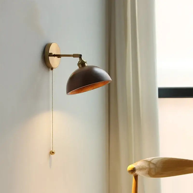 Walnut and brass wall sconce with dark bronze dome shade, adjustable arm, and pull chain switch for bedroom lighting