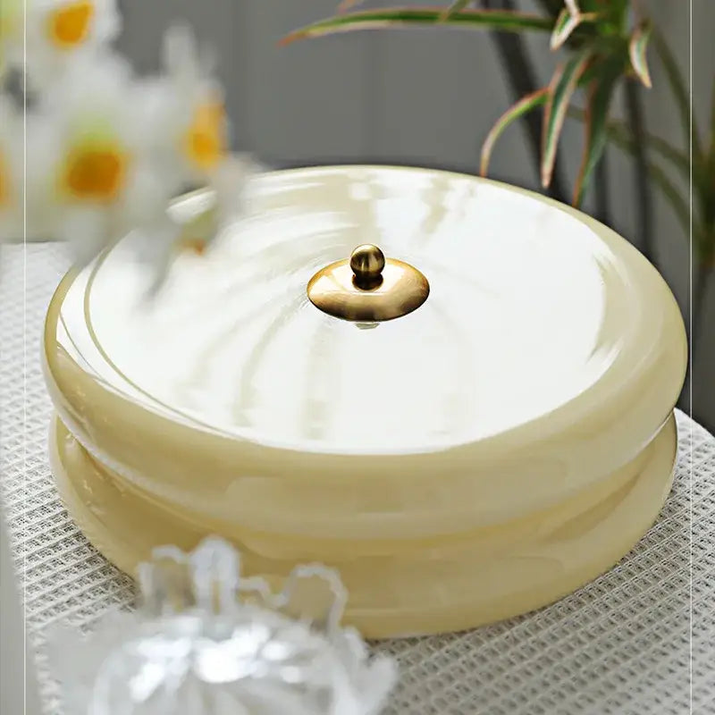 Cream-colored ceramic round lidded container with gold knob next to warm chrome double layer glass led ceiling light