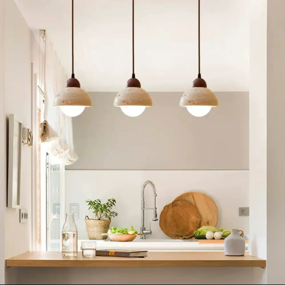 Three beige textured ceramic decorbites cave stone pendant lights with dark brown cords above a kitchen counter
