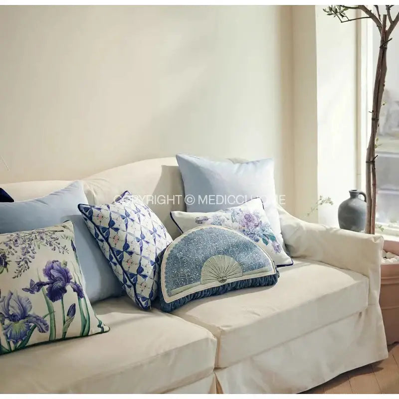 A soft cream-colored sofa with decorbites iris flowers butterfly purple cushion cover and assorted blue white pillows